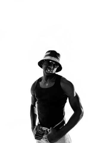 A stylish man in sunglasses and a bucket hat strikes a confident pose in a high-contrast black and white studio shot.