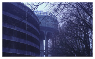 A moody view of an urban landscape with a large curved building and viaduct surrounded by bare trees.