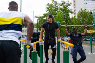 A group of men working out on exercise equipment in an urban park setting.
