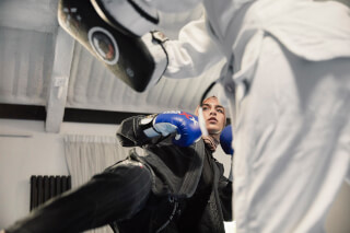 A woman wearing a hijab practices taekwondo with a trainer in a gym setting, demonstrating fitness and determination.