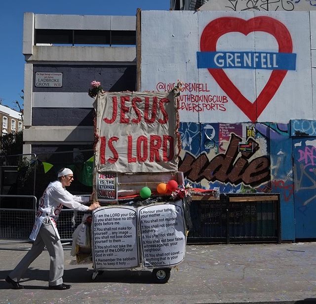 A man pushes a cart with religious signs and a memorial near the Grenfell Tower mural.