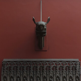 A historical gargoyle sculpture mounted on a red wall, evoking classic and contemplative tones.