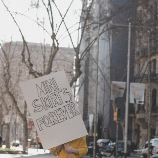 A person holds a sign that reads 'Mini Skirts Forever' on a city street.