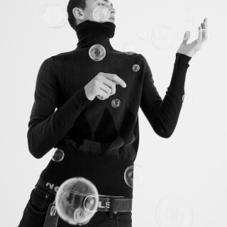 Black and white studio portrait of a man surrounded by floating soap bubbles.