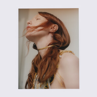 Elegant woman with red hair wearing a gold necklace looking up in a dreamy light for fashion and beauty campaigns.