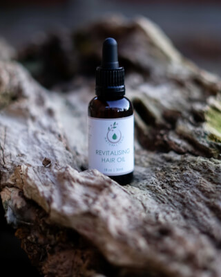 A bottle of revitalizing hair oil sits on a piece of wood.