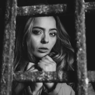 A woman is seen behind bars in a black and white portrait, creating a moody and emotional image.