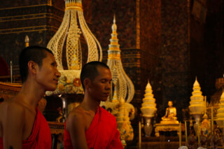 Two buddhist monks in red robes are in a temple setting for prayer and meditation.