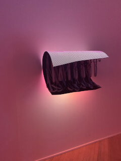 Modern art installation featuring draped ribbons and a glowing LED panel creates a moody and contemplative atmosphere.