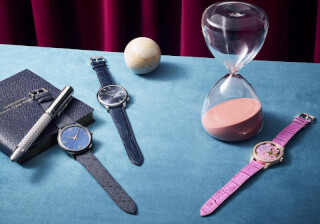 Elegant still life featuring watches, a pen, and an hourglass on a soft blue surface.