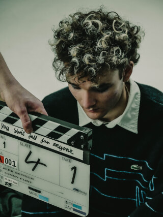 A man gazes downward next to a film slate, set for take 1. Scene 4 in an editorial style.