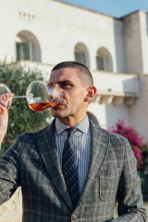 A sophisticated man in a suit is tasting rose wine outdoors during the day.
