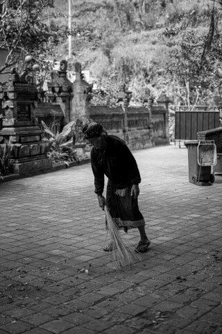 A Balinese woman sweeps the temple grounds in a black and white documentary style photo.