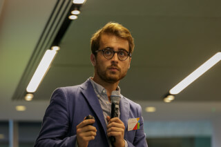 A confident man presents with a microphone in a modern office setting, suitable for business and leadership presentations.