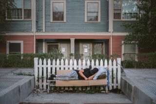 A homeless man sleeps on a makeshift bed in an urban setting, highlighting social issues and community challenges.