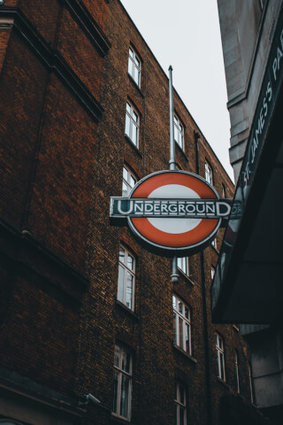 A London Underground sign hangs outside a brick building in an urban environment.