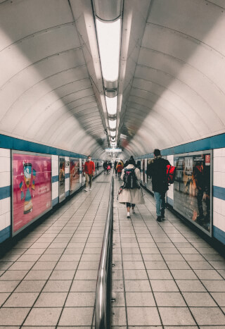 People walk through a long underground tunnel with advertisements and lighting, showcasing urban public transportation.