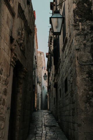 A narrow cobblestone alleyway lined with stone buildings and hanging lamps creates a timeless urban scene.