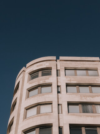 Low-angle shot of a building with a rounded corner against a clear blue sky, emphasizing modern architecture and urban design.