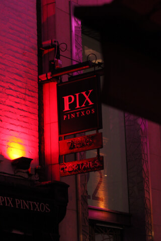 A vibrant red-lit restaurant sign "Pix Pintxos" advertising tapas and cocktails in an urban setting.
