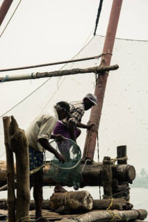 Two fishermen work on a traditional Chinese fishing net platform, preparing for a day of fishing.