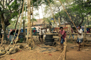 Men use a rope system with tires for lifting in an outdoor setting, showcasing traditional labor and local culture.