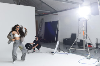 A fashionable woman poses in a studio while an assistant uses a fan to create movement for a dynamic shot.