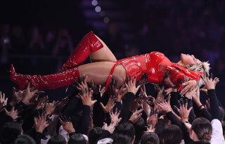 Singer Bebe Rexha is crowd surfing while performing on stage at a concert in front of a big crowd.