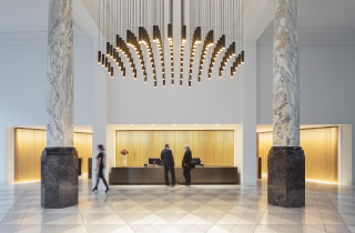 A bright, modern hotel lobby features a reception desk and unique chandelier, creating an elegant welcome for guests.