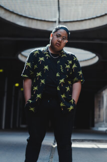 A man in a tropical shirt stands confidently in an urban tunnel setting.
