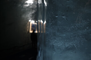 A person explores the mysterious depths of a dimly lit ice tunnel, highlighting the textures of the ice.