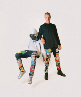 Two men showcasing comic book themed fashion in a studio setting against a plain background.