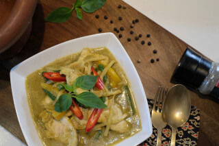 Overhead shot of chicken green curry with bamboo shoots, peppers, and basil, served on a wooden board.