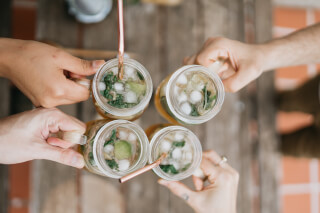 Four people toasting with drinks in mason jars at a party.