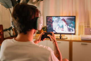 A man with headphones plays a video game with a controller in a cozy living room setting.