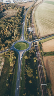 Aerial view showcases a roundabout connecting roads and a railway line in a rural countryside setting.