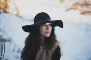 A woman in a fur vest and hat gazes thoughtfully into the distance in a snowy winter scene.