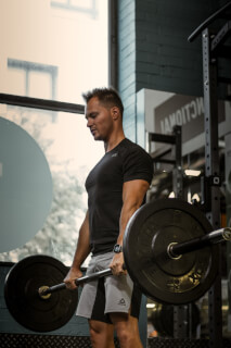 A fit man lifts a barbell during a weightlifting workout in a gym. Promoting fitness and active lifestyle.