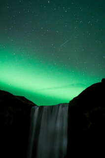 A mesmerizing view of a waterfall beneath a starry sky illuminated by vibrant green northern lights.