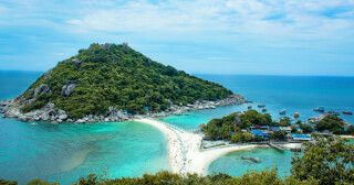 Aerial view of a tropical island with a sandbar and many people enjoying a sunny day at the beach.