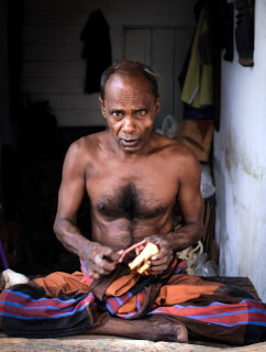 An older man sits indoors, preparing food. This image depicts domestic life and cultural traditions.