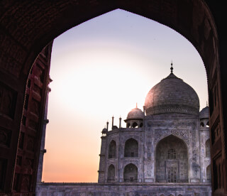 The Taj Mahal, a marble mausoleum in Agra, India, is framed by an archway at sunset, showcasing its serene beauty.