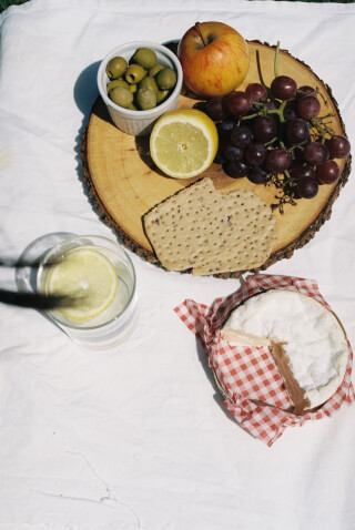 An inviting picnic spread with cheese, fruit, and drinks on a white blanket, perfect for a sunny outdoor meal.