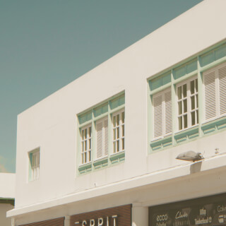 Modern building facade with clean lines and pastel colors, featuring various brand logos on the storefront.