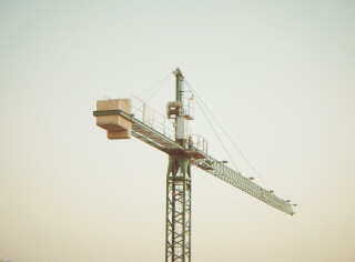 A green construction crane stands tall against a neutral sky, ready for building and development.