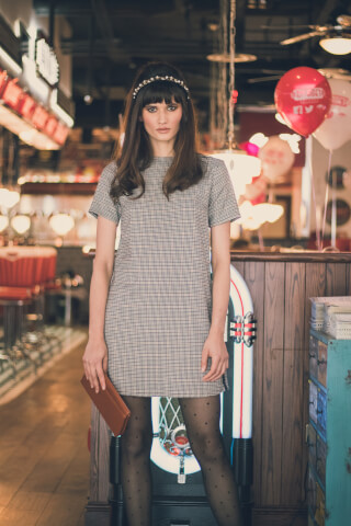 A woman in a vintage-style dress stands in a retro diner, holding a clutch. Perfect for editorial and advertising.