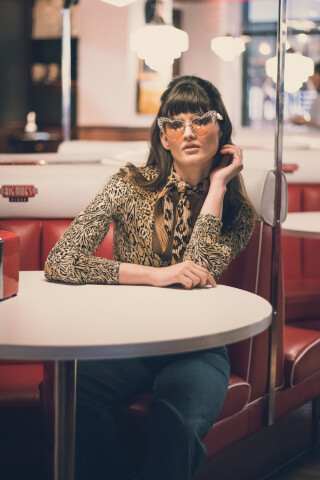 A stylish woman with heart-shaped sunglasses sits in a retro diner booth.