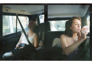 Two women inside a car, one sleeping and the other applying makeup during a ride.