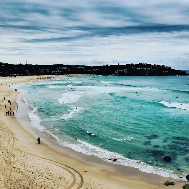 A vibrant beach scene featuring people enjoying the waves and sandy shore under a cloudy sky.