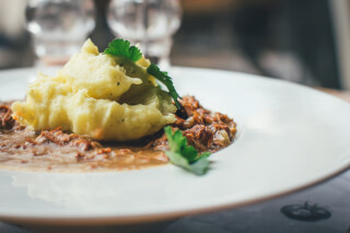Mashed potatoes and meat dish with parsley on a white plate, showcasing gourmet comfort food.